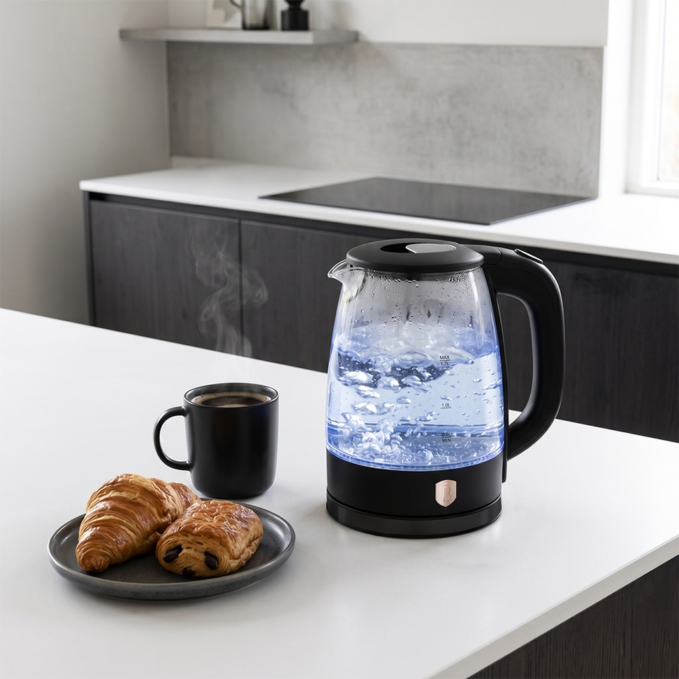 Electric kettle on a white kitchen island with steam, beside a black mug and a plate of croissants and pastries.