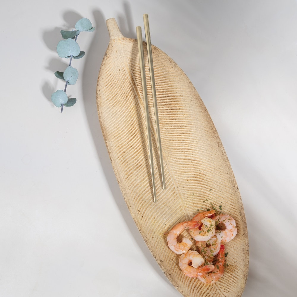 Leaf-shaped textured plate with shrimp curled in a ring, paired with chopsticks and a sprig of eucalyptus on the side.