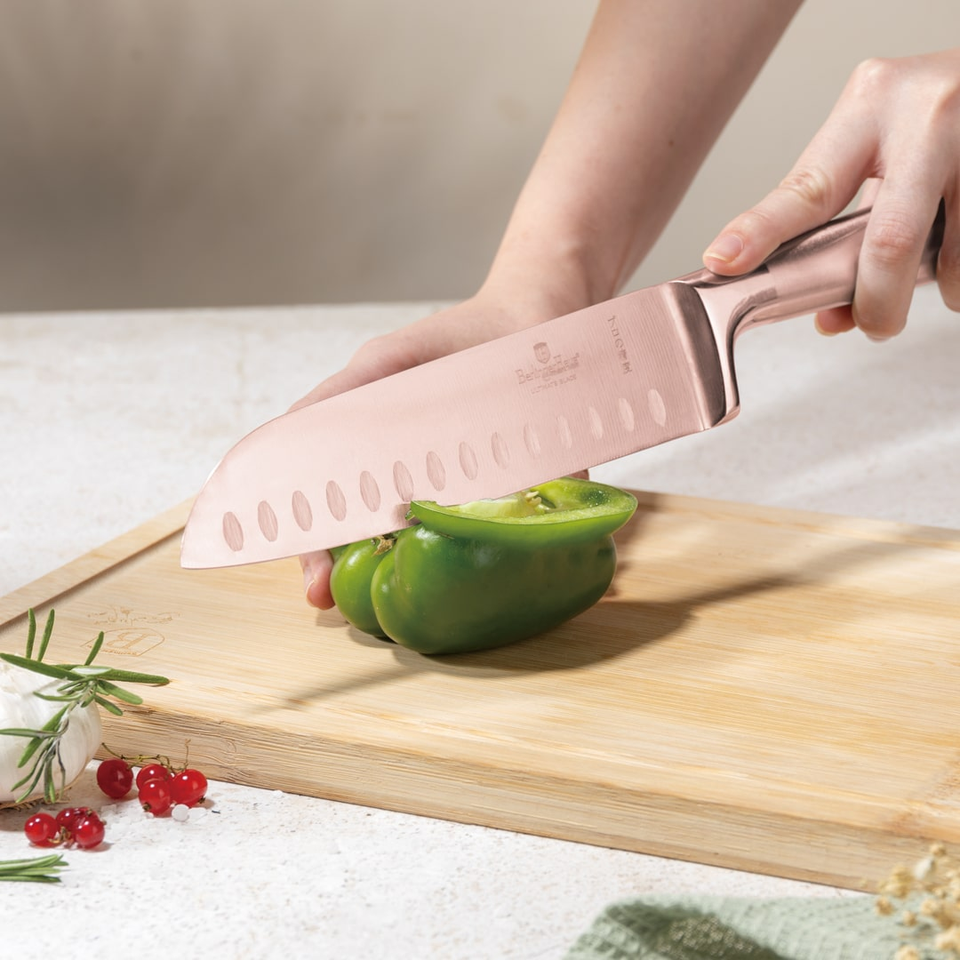 Person slicing a green bell pepper on a wooden cutting board with a pink knife.