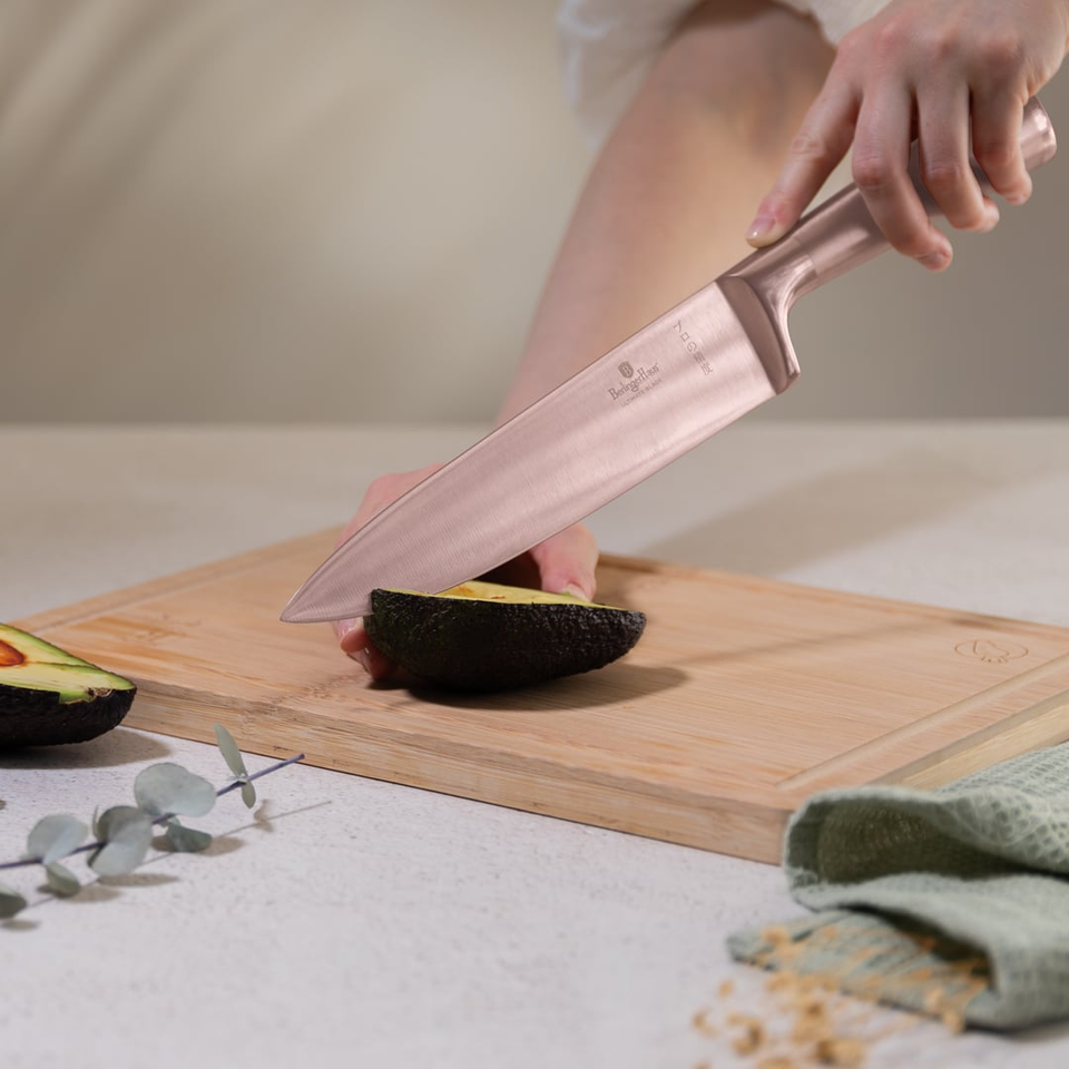 Person slicing a ripe avocado in half on a wooden cutting board with a large knife on a kitchen counter