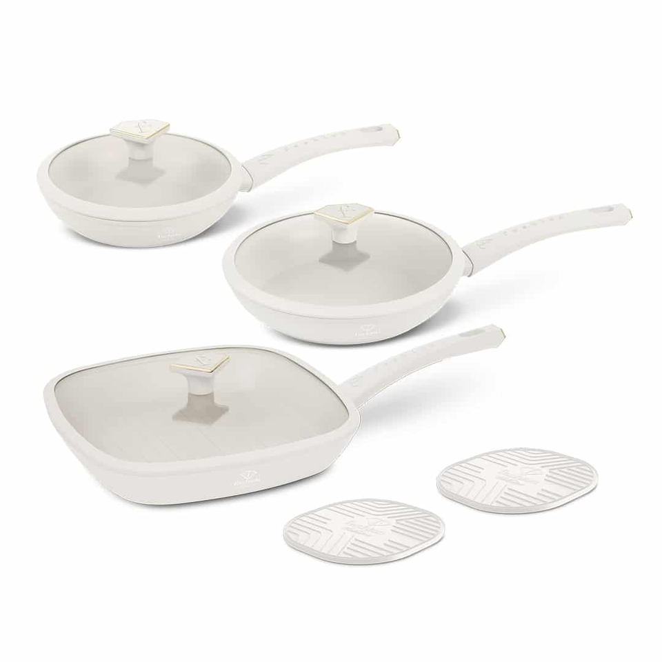 White nonstick cookware set with three pans and glass lids, each with long white handles, plus two circular white trivets.