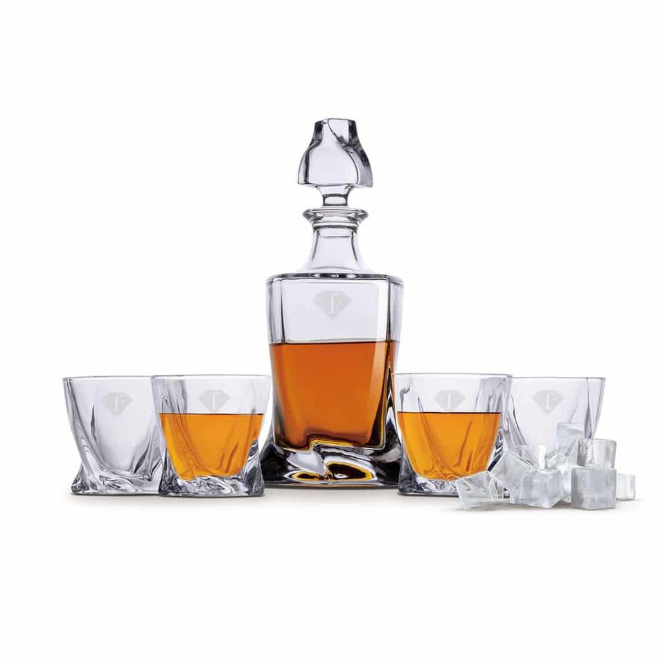 Crystal whiskey decanter with amber liquid, flanked by four crystal glasses and scattered ice cubes on a white background.