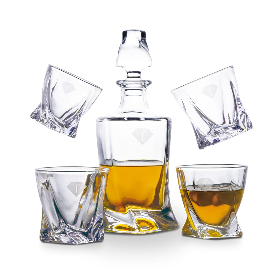 Crystal whiskey decanter with amber liquid surrounded by four crystal glasses on a white background.